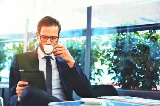 Portrait of handsome successful man drink coffee and look to the digital tablet screen sitting in coffee shop, business man having breakfast sitting on beautiful terrace with plants